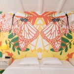 Colorful bedroom inside a Papagayo Curaçao resort villa featuring a bold mural of orange monarch butterflies and tropical foliage above a double bed with white linens and yellow lamps.*