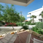Terrace of a garden view room at Papagayo Curaçao with lounge chairs overlooking a lush, landscaped courtyard with palm trees, flowering shrubs, and modern architecture.