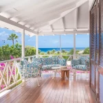Charming Caribbean-style villa at Papagayo Curaçao featuring colorful patterned lounge chairs, wooden flooring, and a stunning ocean view surrounded by lush tropical gardens.