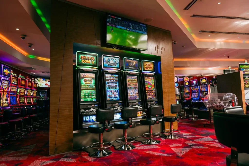 Colorful slot machines and bar stools at Diamonds Casino inside Papagayo Hotel, with a TV playing sports in a vibrant gaming atmosphere