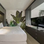 Modern hotel room at Papagayo Beach Hotel featuring a king-size bed, flat-screen TV, and a tropical leaf mural on the wall.