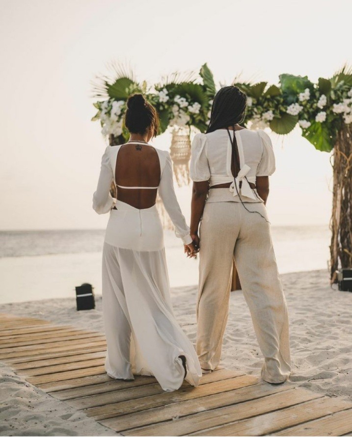 Papagayo Hotel Occasions Two women holding hands, walking towards a beautifully decorated beach altar at sunset for a romantic ceremony at Papagayo.