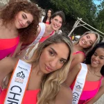 Behind-the-scenes selfie of Miss Netherlands contestants in bright swimsuits, smiling and enjoying a beach photoshoot at Papagayo Beach Curaçao.