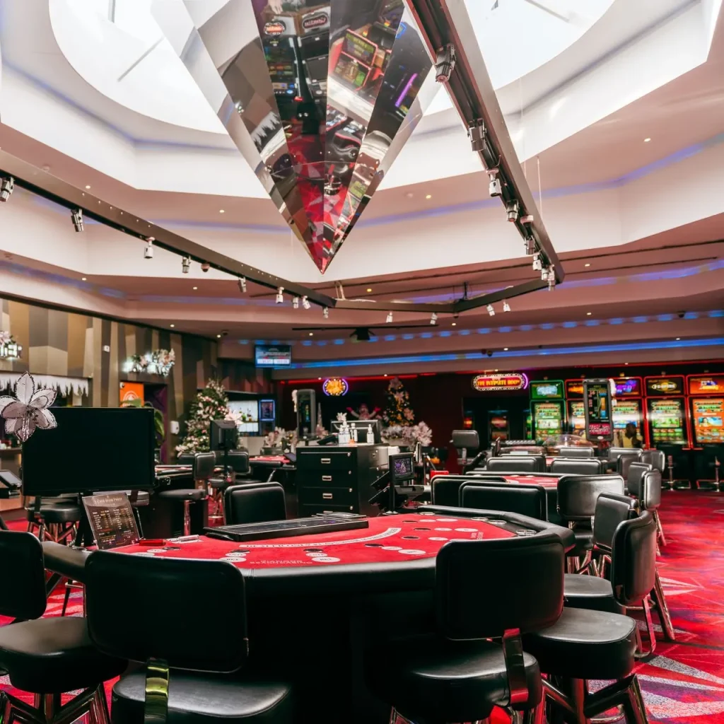 Interior view of Diamond Beach Casino at Papagayo Hotel, featuring vibrant slot machines, gaming tables, and neon lighting under a skylight ceiling.