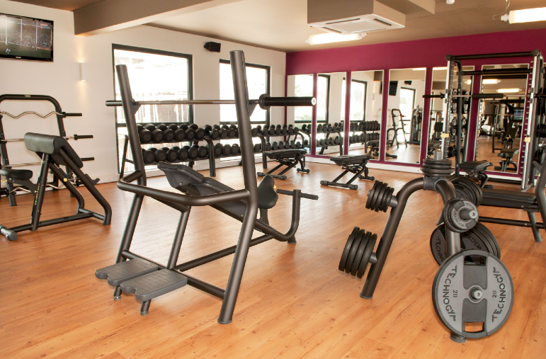 The Challenge Gym Papagayo Hotel Spacious and modern gym with strength training equipment, dumbbells, weight plates, and mirrors at The Challenge Gym in Papagayo Hotel.