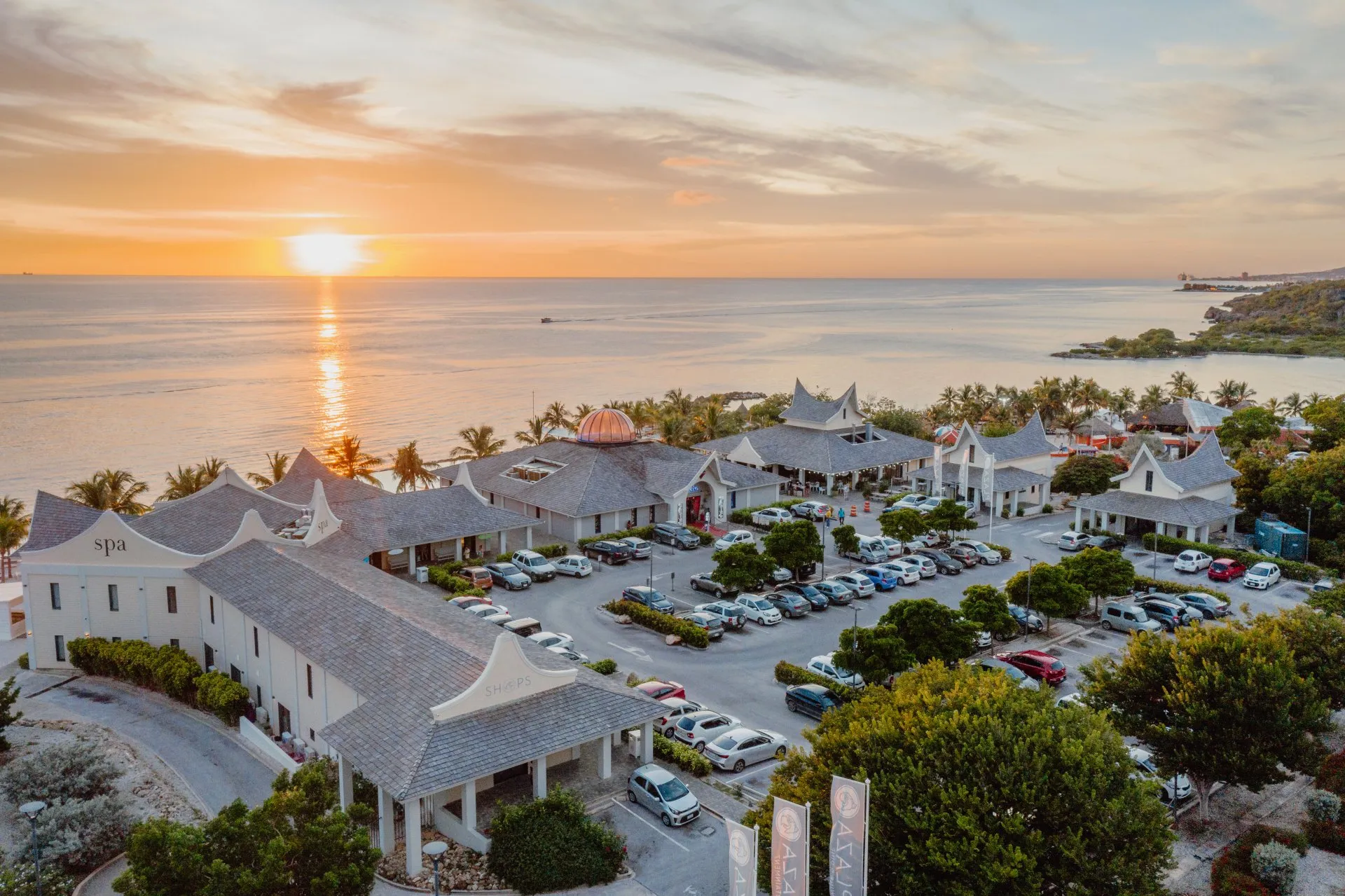Aerial view of Papagayo Plaza at sunset, with a central dome building, surrounding shops, and palm-lined beachfront along the Caribbean Sea.
