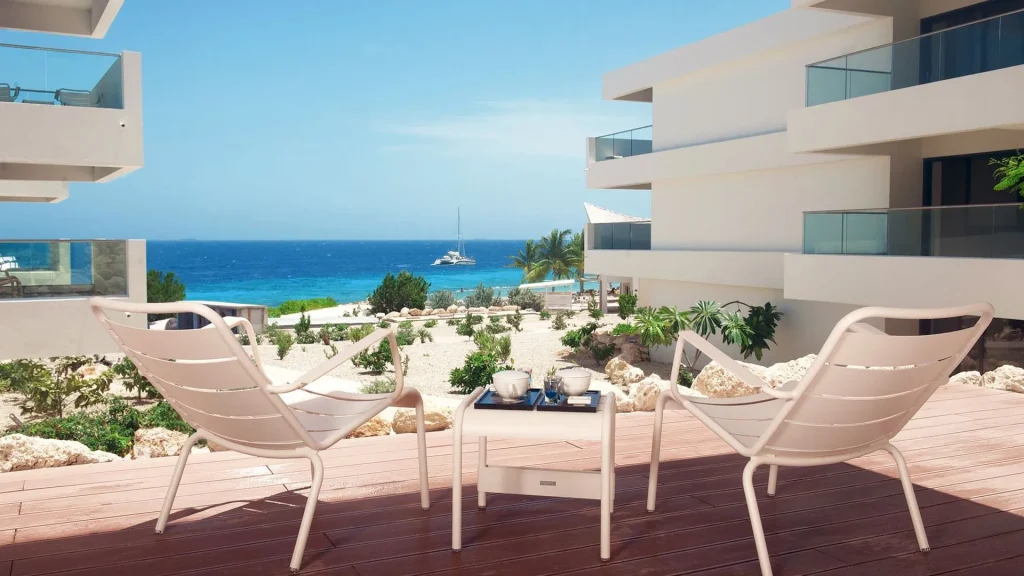 Oceanfront terrace view from Papagayo Beach Hotel featuring modern lounge chairs, a coffee table setup, and a catamaran sailing in the turquoise Caribbean Sea.