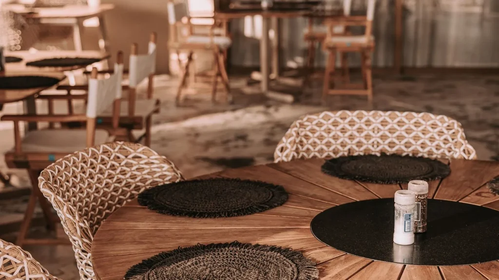 Elegant outdoor dining area at Papagayo Curaçao featuring a round wooden table with woven chairs, black placemats, and soft ambient lighting during golden hour.