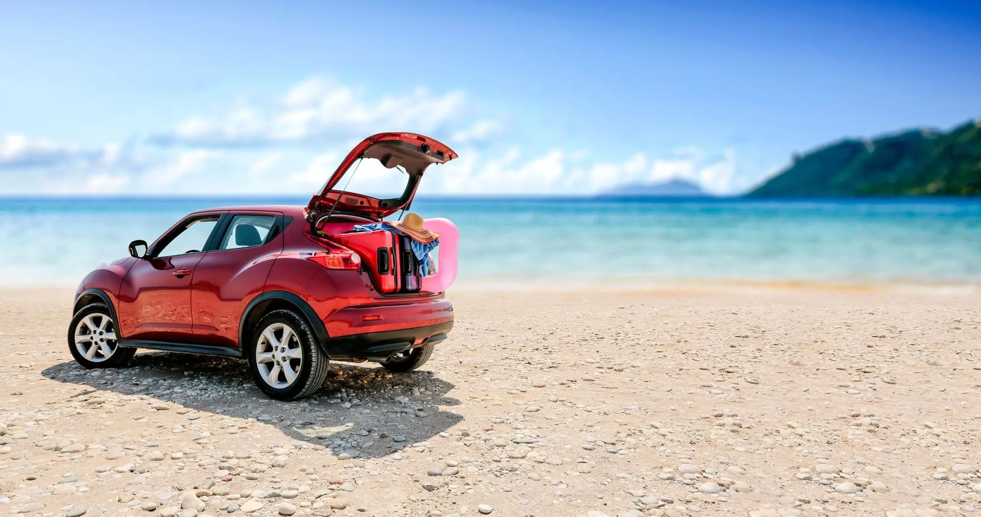PapagayoBeach Hotel Car Rental Rental car parked on a sandy beach with its trunk open, packed with vacation gear and beach accessories, overlooking turquoise waters and a scenic coastal backdrop