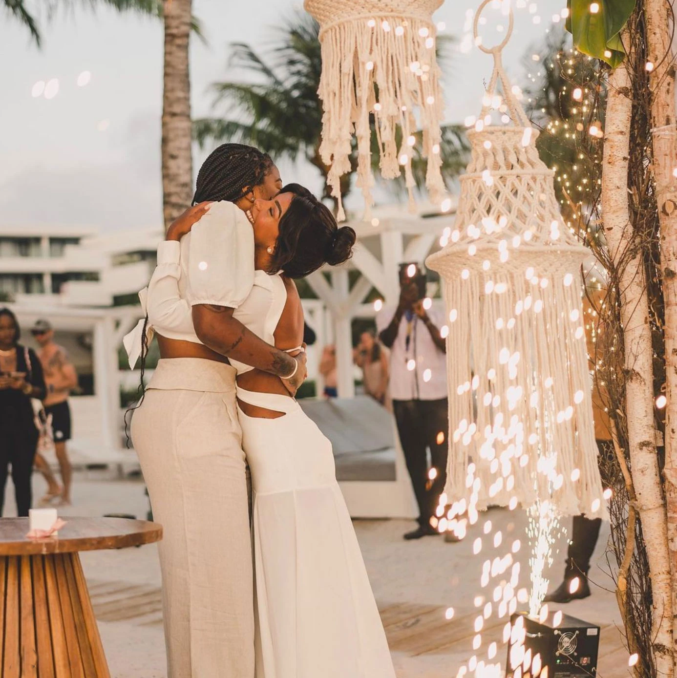 Papagayo Beach Club Beach wedding Two brides embrace under glowing macrame lanterns and sparklers during a beachfront wedding celebration at Papagayo Beach Club.