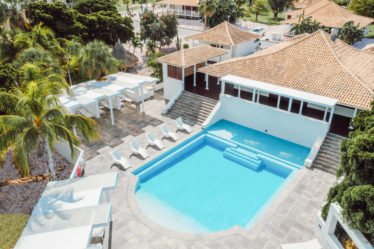 Papagayo Beach Resort Private Pool Aerial view of Papagayo Beach Resort’s serene swimming pool, surrounded by palm trees, shaded seating areas, and terracotta-roofed buildings.