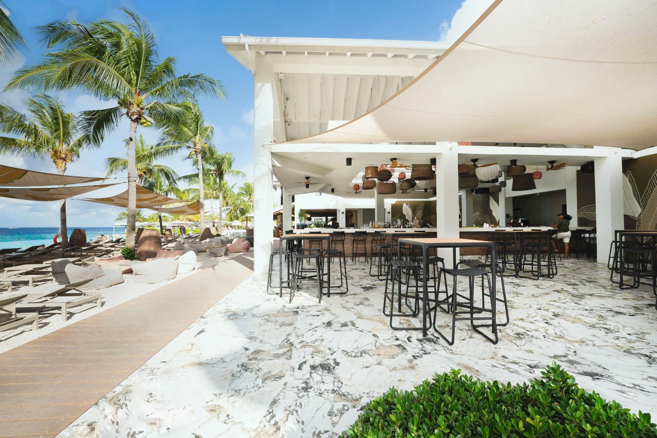 Open-air bar and dining area at Papagayo Beach Club with marble floors, shaded seating, and a view of sun loungers along the white sand beach.