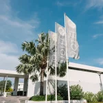 Tall branded Papagayo Beach Hotel flags wave beside palm trees at the resort’s main entrance.