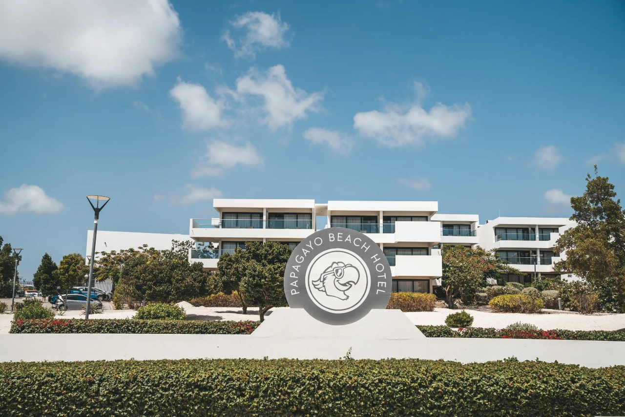 Exterior view of Papagayo Beach Hotel with its iconic parrot logo sign against a clear blue sky.