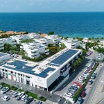 Stunning aerial shot of Papagayo Beach Plaza and Papagayo Beach Hotel, with solar-panelled rooftops, modern white buildings, and the Caribbean Sea in the background.