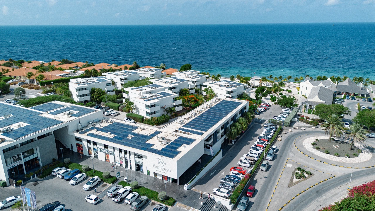 Stunning aerial shot of Papagayo Beach Plaza and Papagayo Beach Hotel, with solar-panelled rooftops, modern white buildings, and the Caribbean Sea in the background.