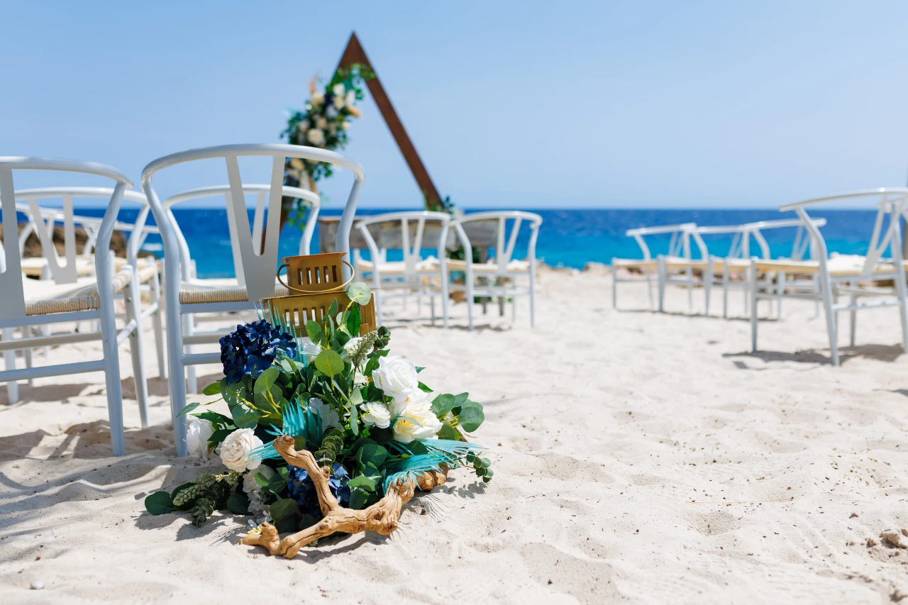 Papagayo Beach Hotel Wedding White chairs and a floral-decorated wooden arch are arranged on the soft sands of Papagayo Beach Hotel, with blue ocean waters providing a stunning backdrop for a beach ceremony.