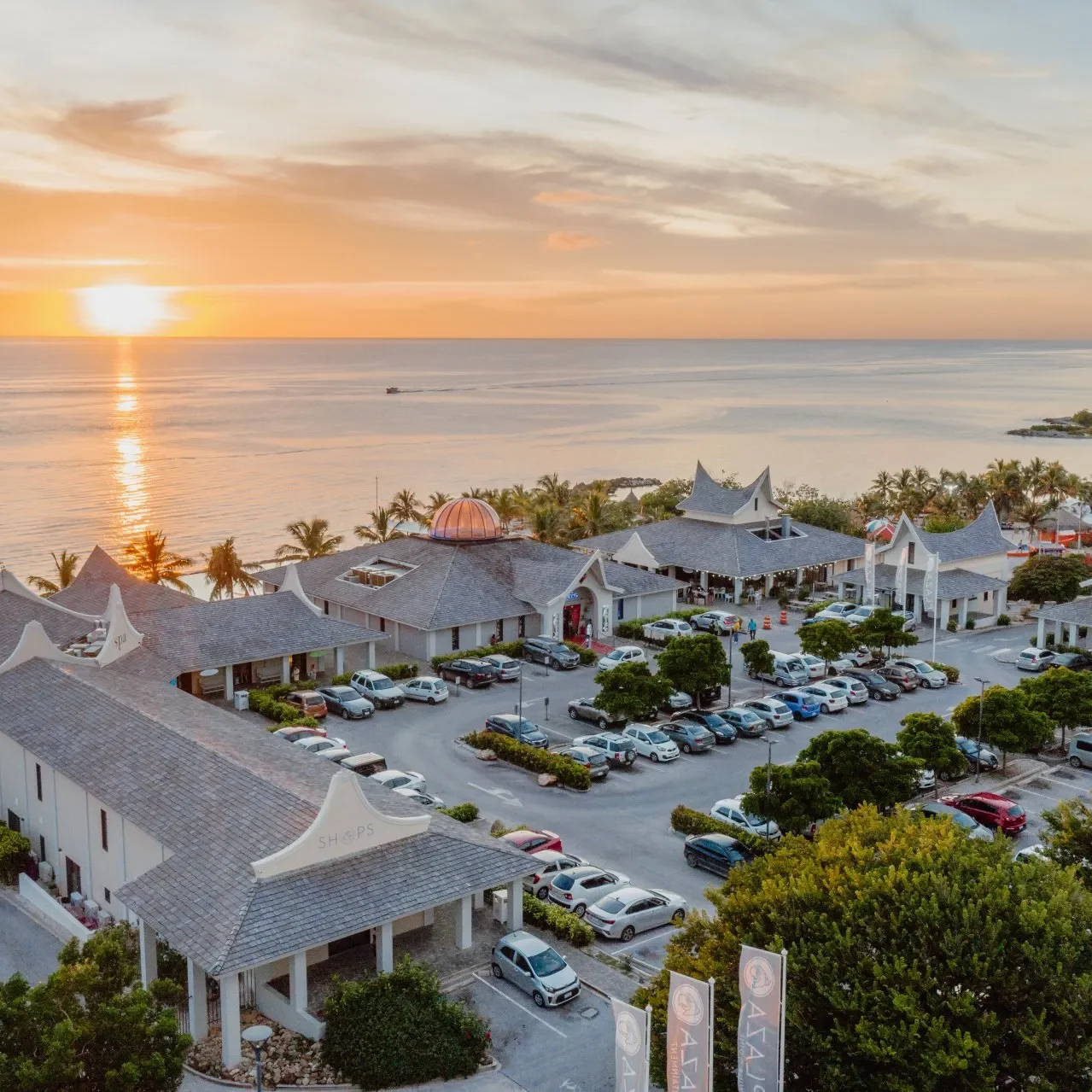 Aerial view of Papagayo Plaza at sunset, with a central dome building, surrounding shops, and palm-lined beachfront along the Caribbean Sea.
